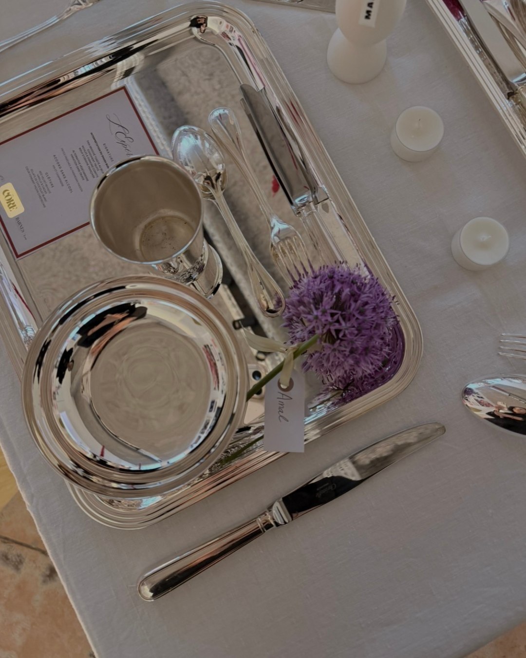 Un couvert nominatif sur son plateau d'argent, le menu, une coupe et une fleur d'allium