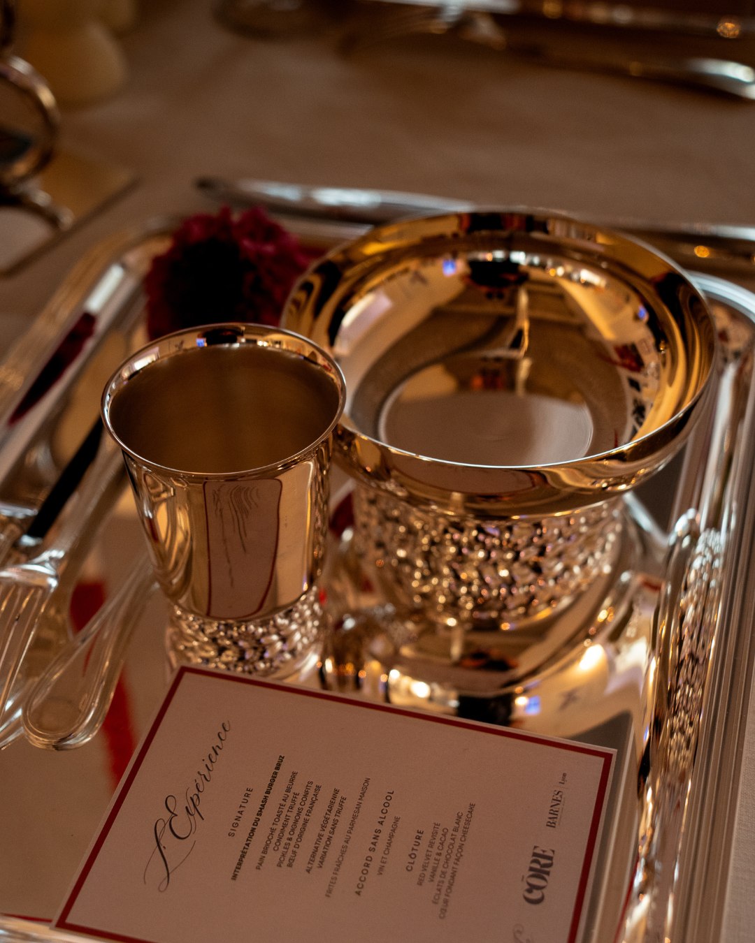 Menu de l'Édition 01 posé sur un plateau d'argenterie Christofle, timbale et coupe éclairées à la bougie