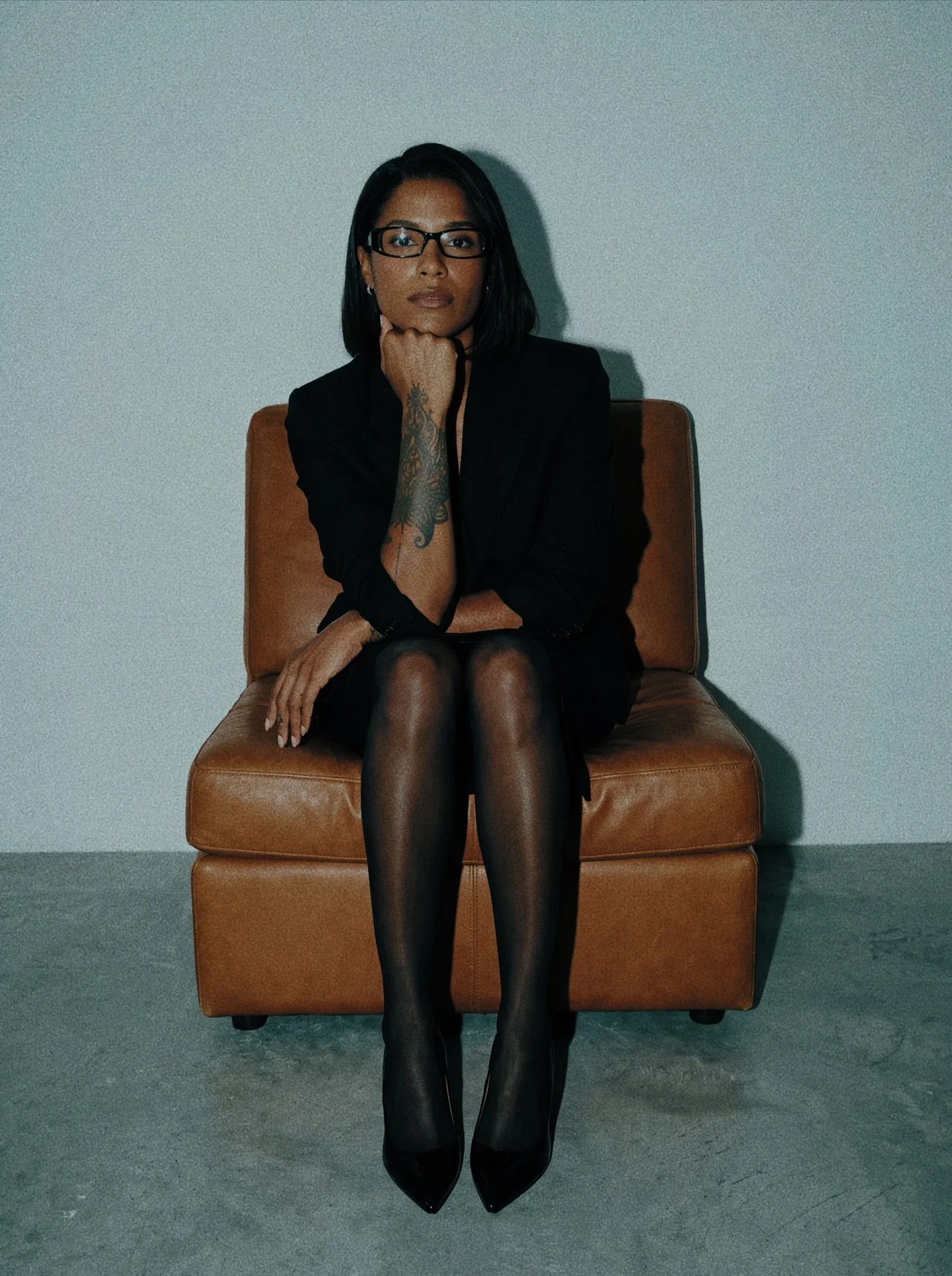 Mélissa Loua, assise dans un fauteuil de cuir brun, veste noire, lunettes, le menton posé sur la main