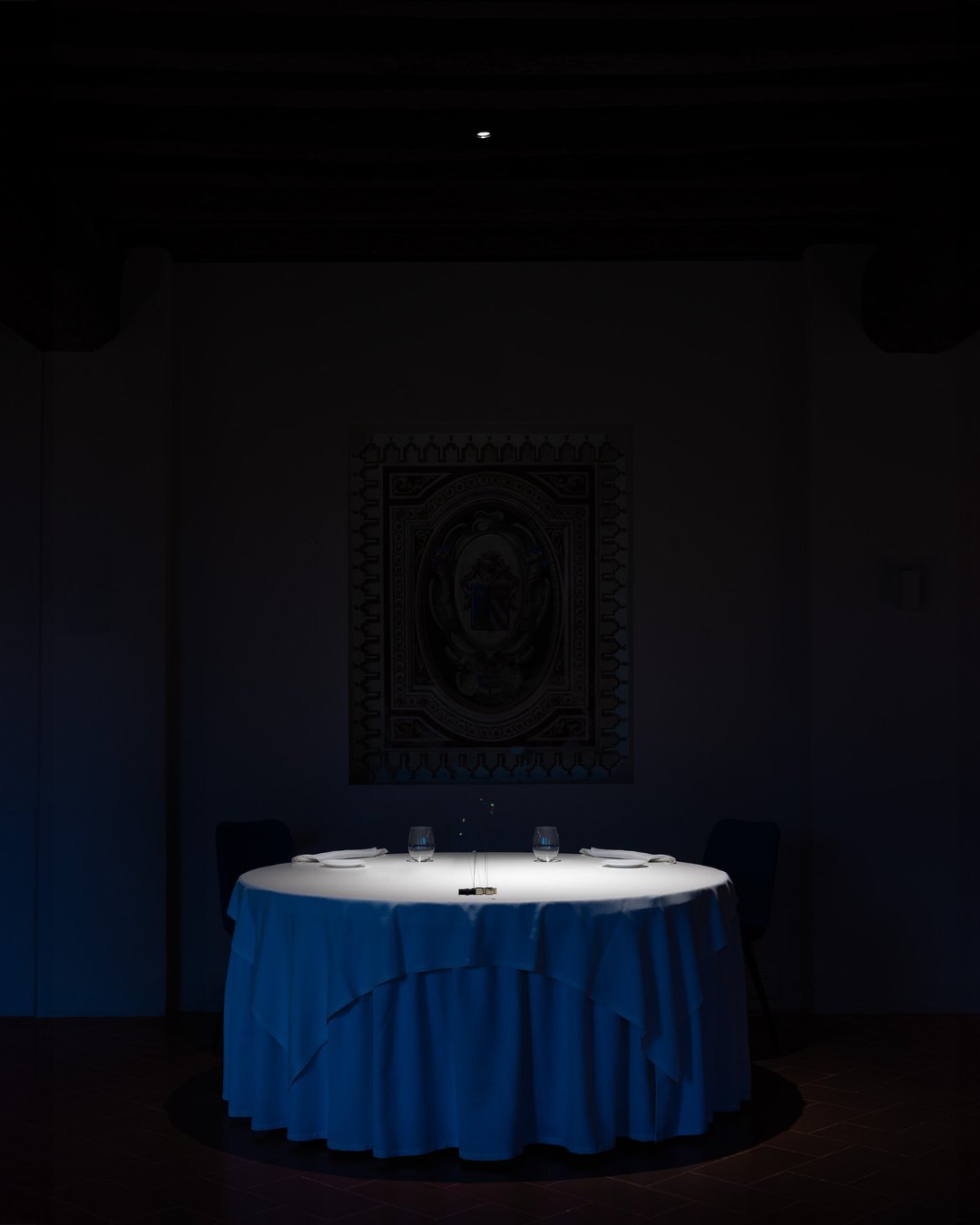 Une table ronde dressée pour deux, éclairée seule au centre d'une salle sombre